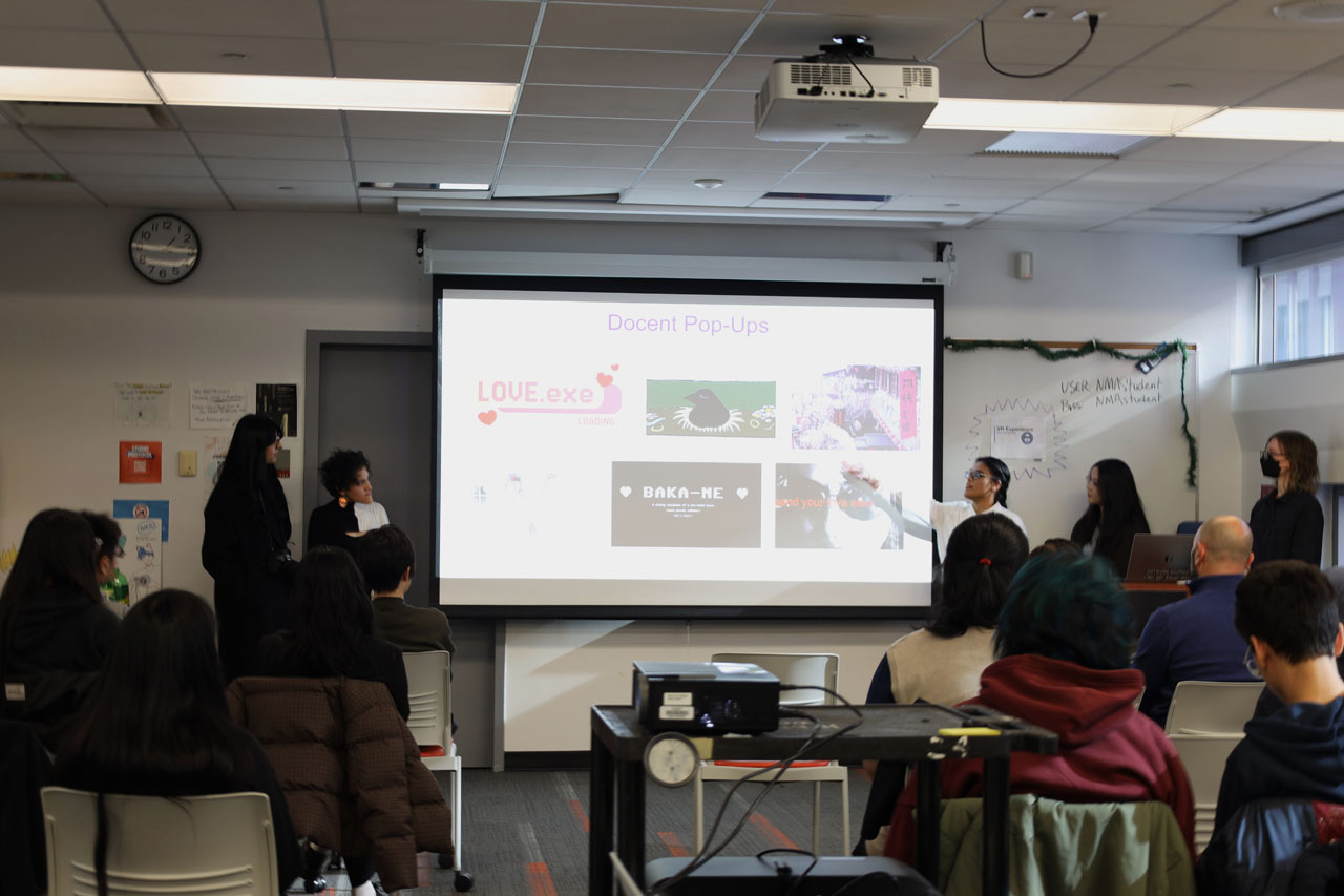 The docents present about Docent Pop-Up exhibitions. LOVE.exe, the summer 2025 exhibition, is on the screen behind them.