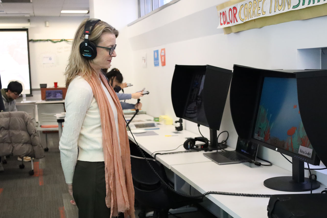A student wearing a headset watches a screen showing student work. The screen shows a cut-out paper animation.
