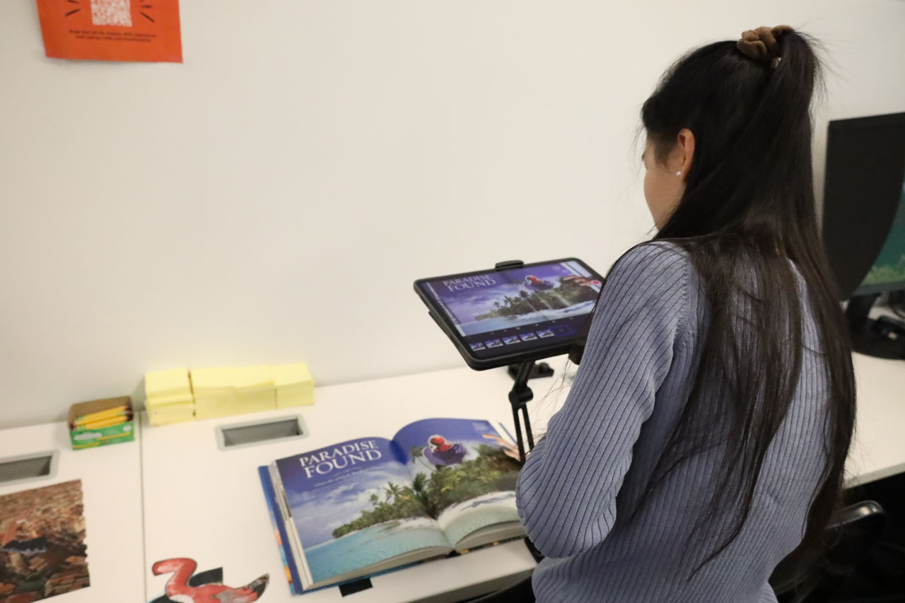 A student uses an iPad on a stand to create a stop-motion animation with collaged materials.