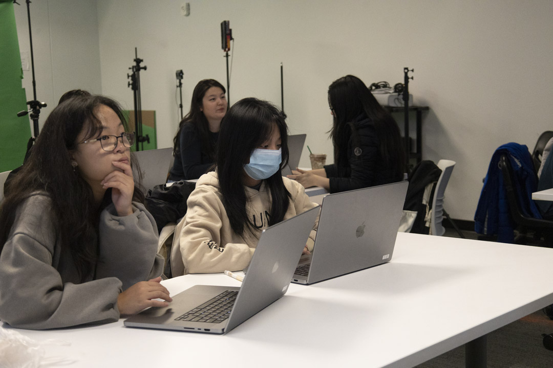 A student holding a prop sword up to the camera. The figure is edited to be neon green, and the background is pink.
