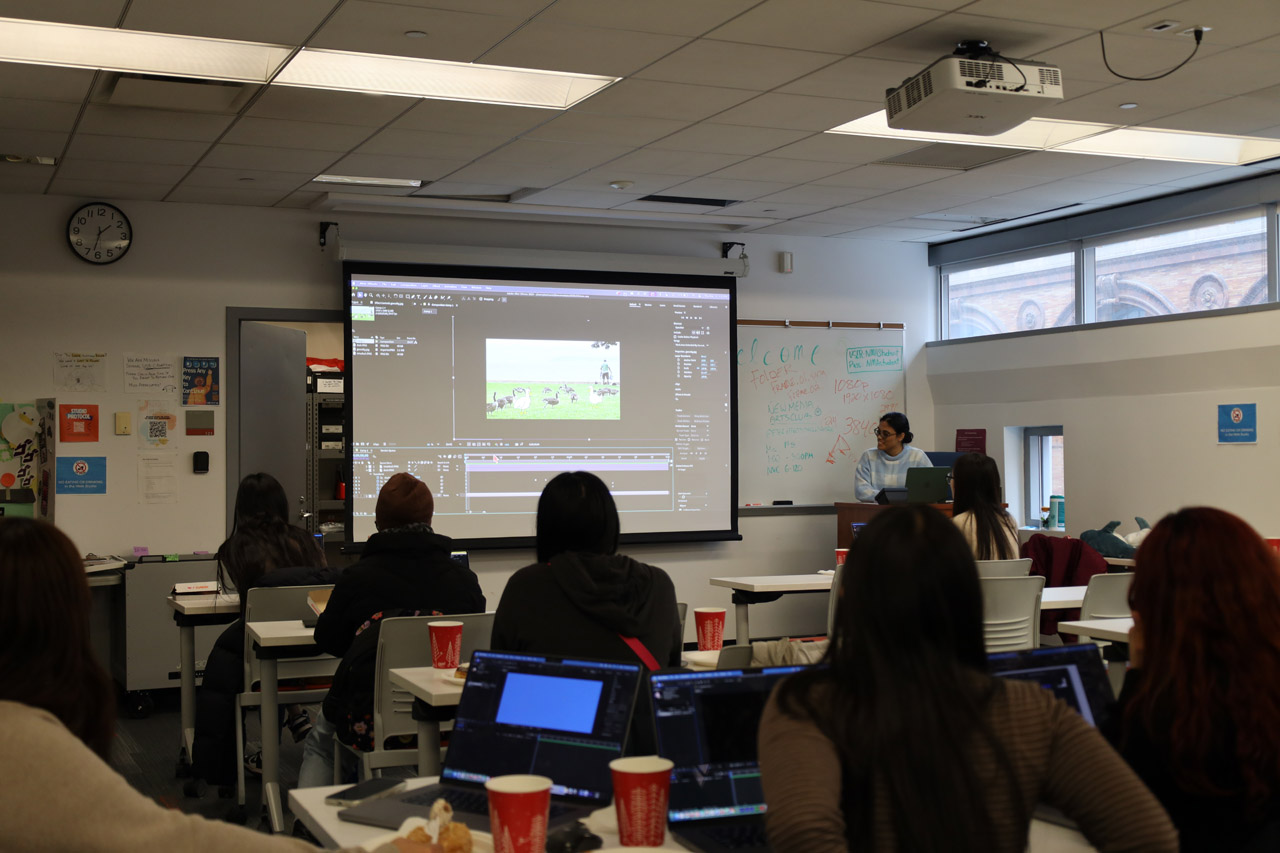 Students working on laptops in the NMA Studio, following an After Effects demo on the screen led by a docent.