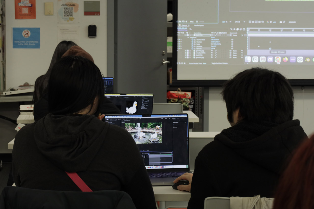 An over-the-shoulder view of two students in the NMA Studio collaborating on an animation in After Effects of a fountain and ducks.