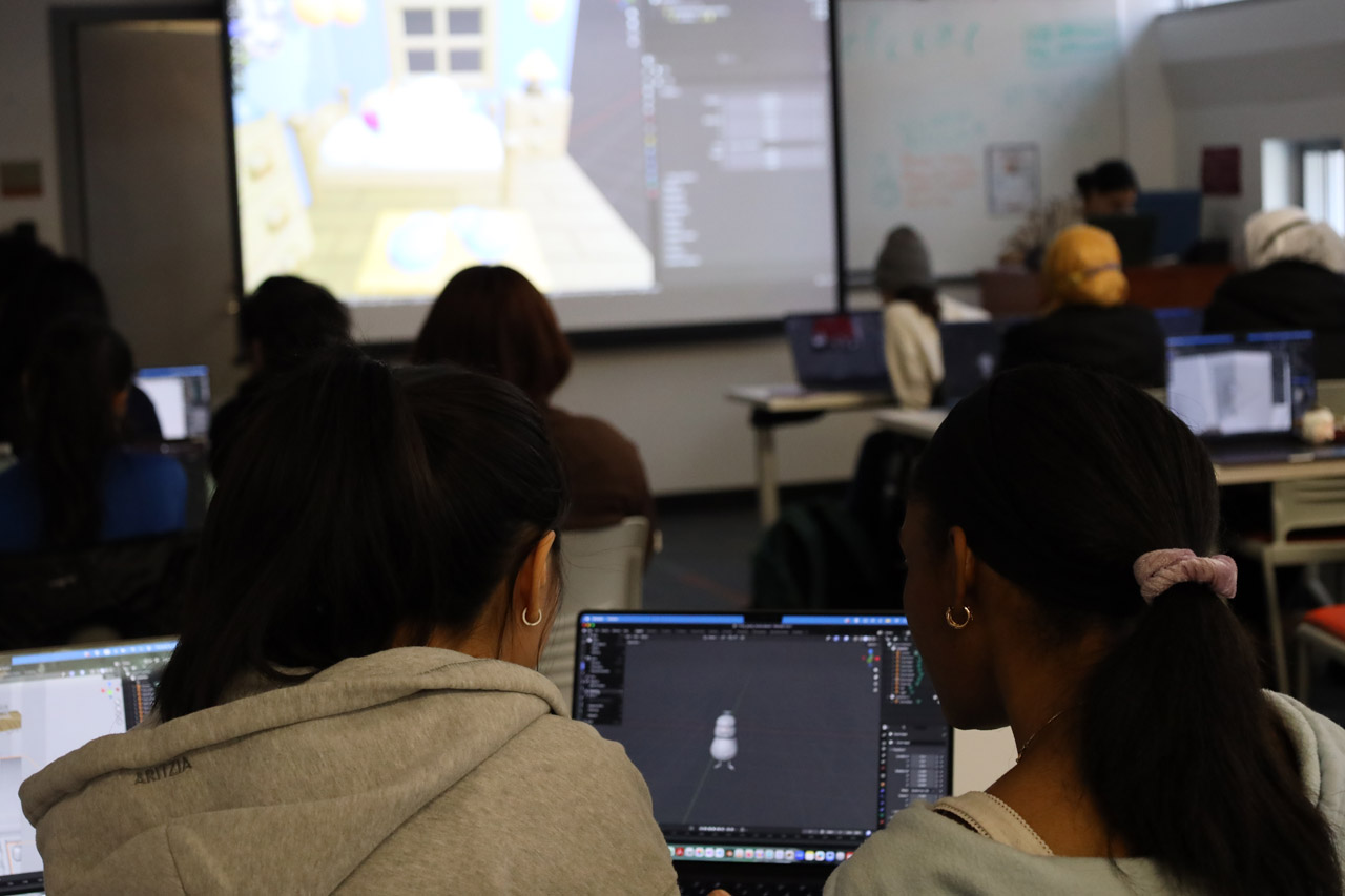 An over-the-shoulder view of two students in the NMA Studio collaborating on a Blender model of a duck.