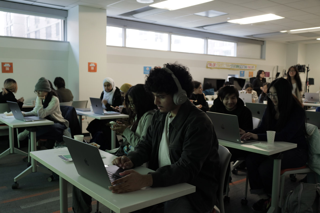 Students working on laptops at rectangular tables.