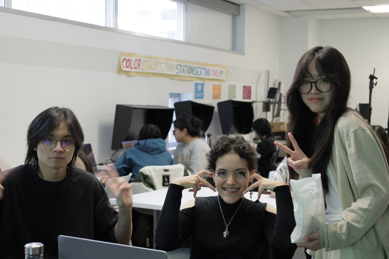 Three students smile for the camera, with the two on the side making peace signs and the middle one making a heart.